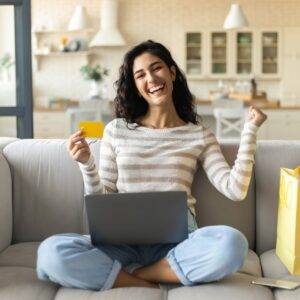 Femme souriante tenant une carte bancaire devant son ordinateur portable