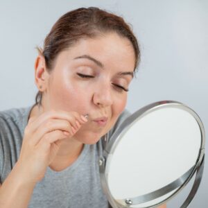 Femme se regardant dans un miroir de table pour s'épiler les poils du visage à la pince à épiler