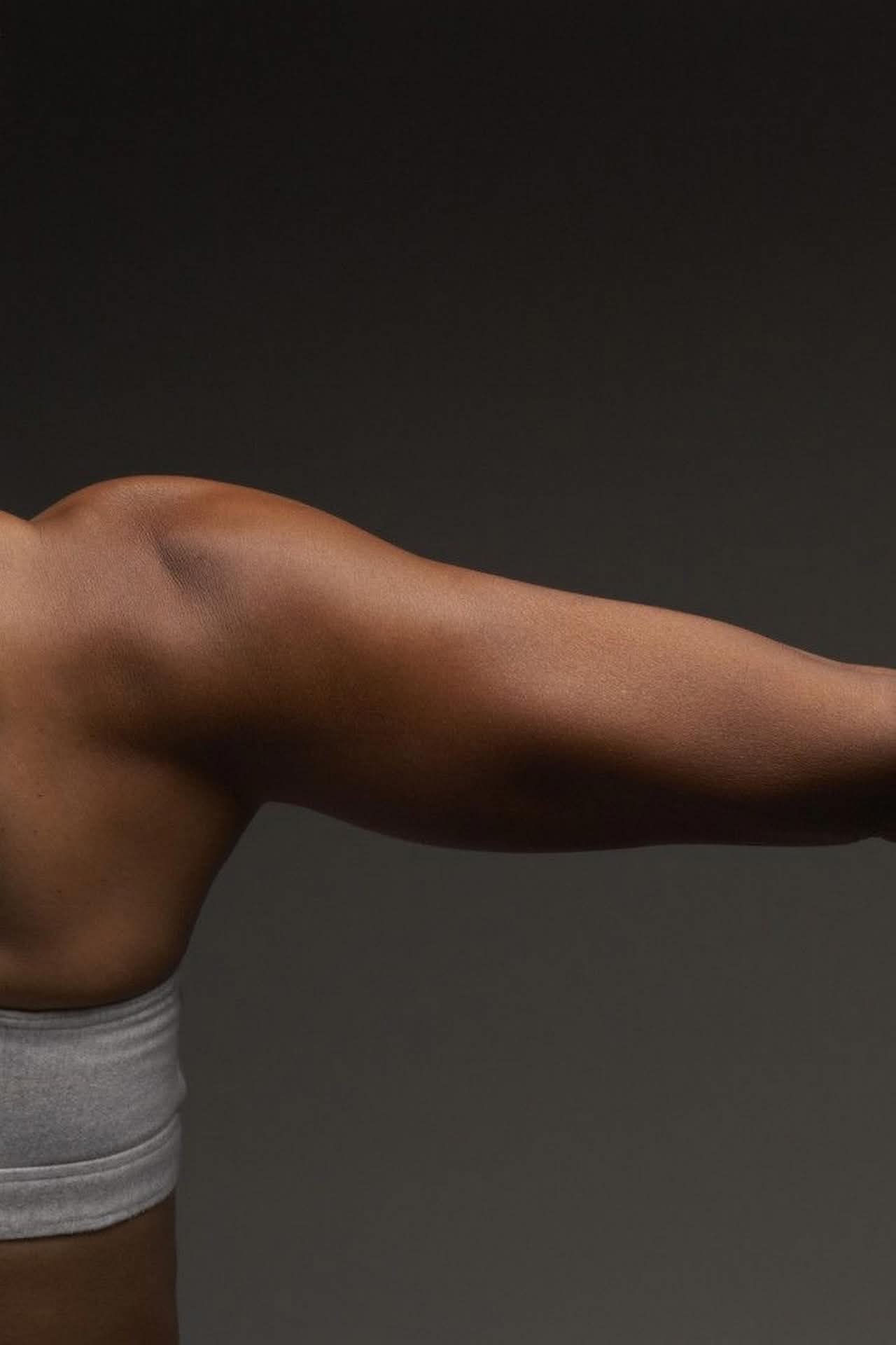 Plan rapproché d'un bras de femme musclé à la peau foncée, l'épaule et le biceps sont fléchis. La personne porte une brassière de sport grise.